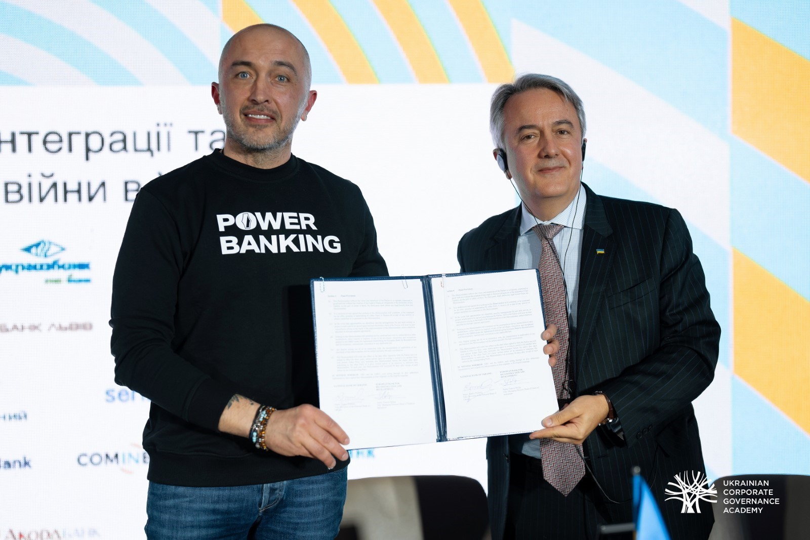 Two people standing on stage holding a certificate while looking at the camera