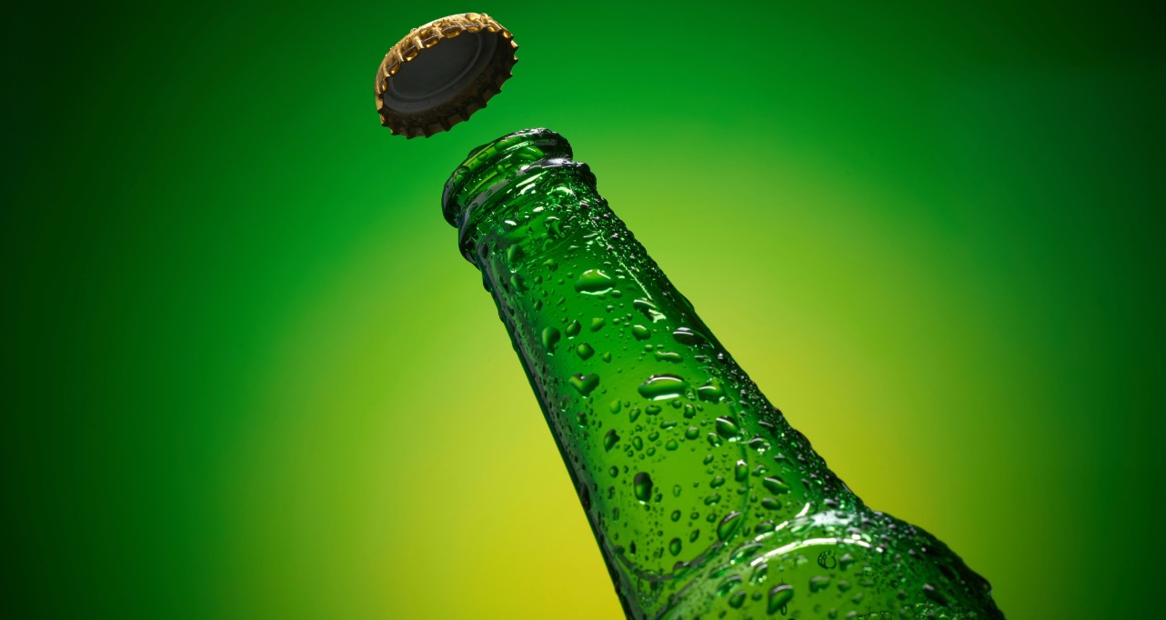 Green cold bottleneck with drops and flying golden cap against yellow green background